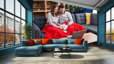 Man and woman watching movie sitting on sofa with dog at home Wall mural