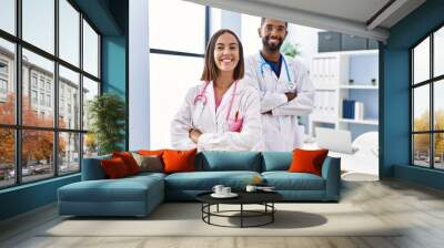 Man and woman wearing doctor uniform smiling confident standing with arms crossed gesture at clinic Wall mural