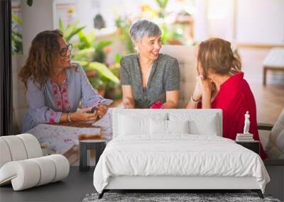 Meeting of middle age women having lunch and drinking coffee. Mature friends smiling happy using smartphone at home on a sunny day Wall mural