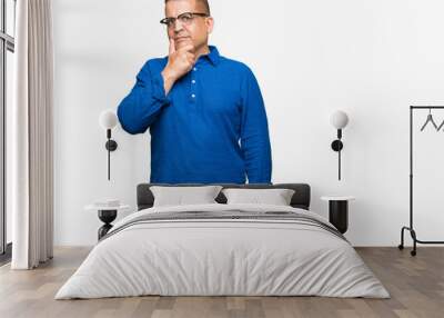 Middle age arab man wearing glasses over isolated background looking confident at the camera with smile with crossed arms and hand raised on chin. Thinking positive. Wall mural