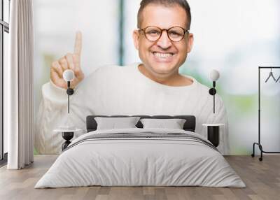 Middle age arab man wearing glasses over isolated background showing and pointing up with finger number one while smiling confident and happy. Wall mural