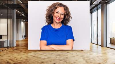 Middle age beautiful brunette woman wearing blue t-shirt standing over white background happy face smiling with crossed arms looking at the camera. Positive person. Wall mural