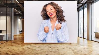 Middle age beautiful brunette woman wearing striped shirt standing over white background celebrating surprised and amazed for success with arms raised and eyes closed Wall mural