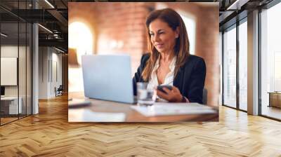 Middle age beautiful businesswoman smiling happy and confident. Sitting on chair working in a desk using smartphone at the office Wall mural