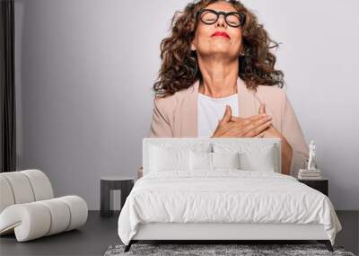 Middle age beautiful businesswoman wearing glasses standing over isolated white background smiling with hands on chest, eyes closed with grateful gesture on face. Health concept. Wall mural