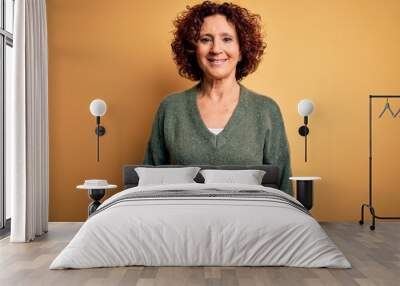 Middle age beautiful curly hair woman wearing casual sweater over isolated yellow background with a happy and cool smile on face. Lucky person. Wall mural