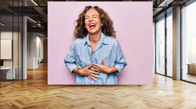 Middle age beautiful woman wearing casual denim shirt standing over pink background smiling and laughing hard out loud because funny crazy joke with hands on body. Wall mural