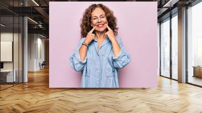 Middle age beautiful woman wearing casual denim shirt standing over pink background Smiling with open mouth, fingers pointing and forcing cheerful smile Wall mural