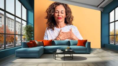 Middle age beautiful woman wearing casual dye t-shirt standing over yellow background smiling with hands on chest, eyes closed with grateful gesture on face. Health concept. Wall mural