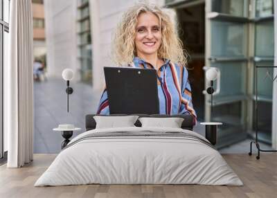 Middle age blonde woman smiling confident holding clipboard at street Wall mural