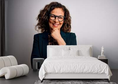 Middle age brunette business woman wearing glasses standing over isolated white background looking confident at the camera smiling with crossed arms and hand raised on chin. Thinking positive. Wall mural