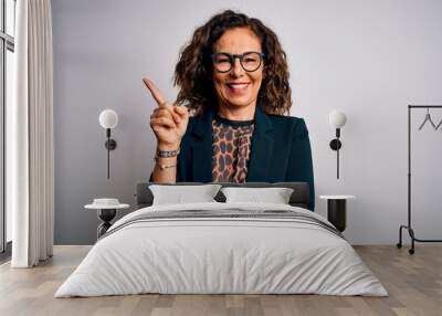 Middle age brunette business woman wearing glasses standing over isolated white background with a big smile on face, pointing with hand and finger to the side looking at the camera. Wall mural