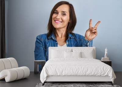 Middle age brunette woman wearing casual denim jacket over isolated background smiling with happy face winking at the camera doing victory sign. number two. Wall mural