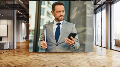 Middle age businessman with serious expression using smartphone at the city. Wall mural