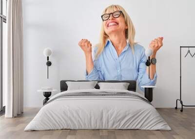 Middle age businesswoman wearing elegant shirt and glasses over isolated white background celebrating surprised and amazed for success with arms raised and eyes closed. Winner concept. Wall mural