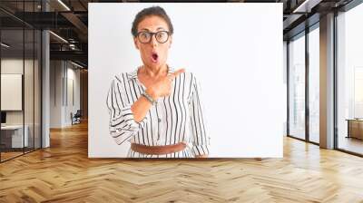 Middle age businesswoman wearing striped dress and glasses over isolated white background Surprised pointing with finger to the side, open mouth amazed expression. Wall mural