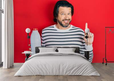 Middle age caucasian man holding liter bottle of milk smiling with an idea or question pointing finger with happy face, number one Wall mural