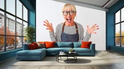 Middle age chef woman wearing apron and glasses over isolated white background celebrating crazy and amazed for success with arms raised and open eyes screaming excited. Winner concept Wall mural