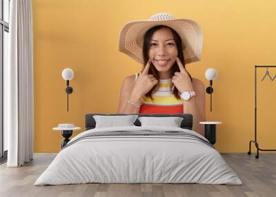 Middle age chinese woman wearing summer hat over yellow background smiling with open mouth, fingers pointing and forcing cheerful smile Wall mural