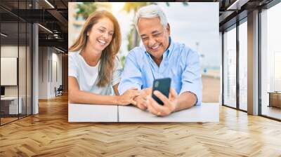 Middle age couple in love sitting at the terrace of coffee shop using smartphone happy and cheerful together Wall mural