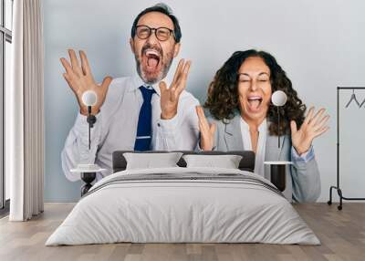 Middle age couple of hispanic woman and man wearing business office uniform celebrating mad and crazy for success with arms raised and closed eyes screaming excited. winner concept Wall mural