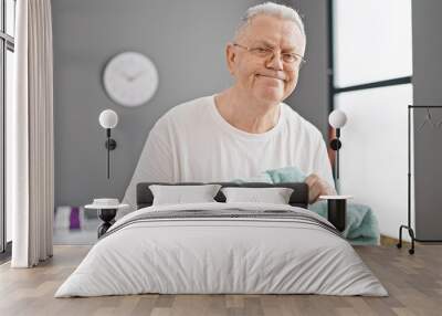 Middle age grey-haired man holding basket smelling clean clothes at laundry room Wall mural