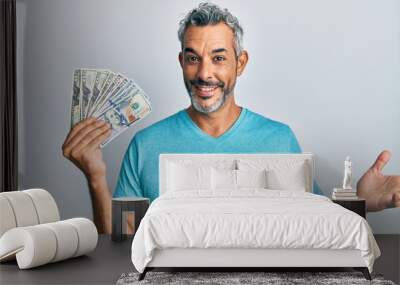 Middle age grey-haired man holding dollars celebrating achievement with happy smile and winner expression with raised hand Wall mural