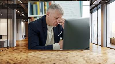 Middle age grey-haired man teacher using computer stressed at university classroom Wall mural