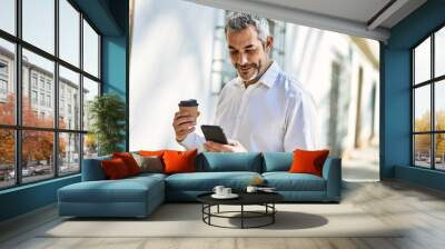 Middle age grey-haired man using smartphone drinking coffee at the city. Wall mural