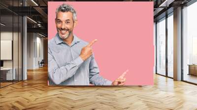 Middle age grey-haired man wearing casual clothes smiling and looking at the camera pointing with two hands and fingers to the side. Wall mural