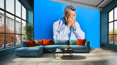 Middle age grey-haired man wearing doctor uniform and stethoscope with sad expression covering face with hands while crying. depression concept. Wall mural