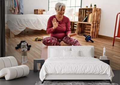 Middle age grey-haired woman training having video call sitting on the floor at bedroom. Wall mural