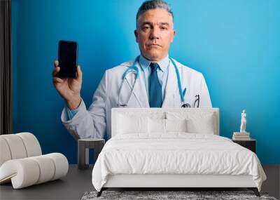 Middle age handsome grey-haired doctor man holding smartphone showing screen with a confident expression on smart face thinking serious Wall mural