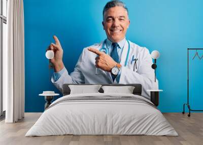 Middle age handsome grey-haired doctor man wearing coat and blue stethoscope smiling and looking at the camera pointing with two hands and fingers to the side. Wall mural