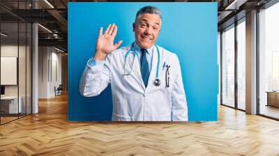 Middle age handsome grey-haired doctor man wearing coat and blue stethoscope Waiving saying hello happy and smiling, friendly welcome gesture Wall mural