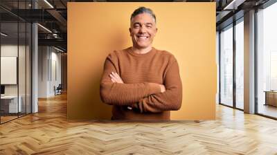 Middle age handsome grey-haired man wearing casual sweater over yellow background happy face smiling with crossed arms looking at the camera. Positive person. Wall mural