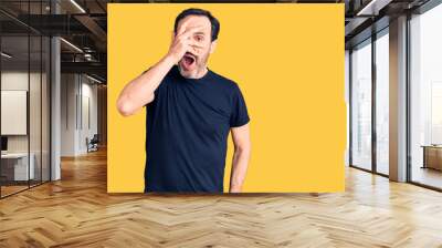 Middle age handsome man wearing casual t-shirt peeking in shock covering face and eyes with hand, looking through fingers with embarrassed expression. Wall mural