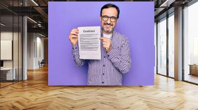 Middle age handsome man wearing glasses holding contract document over purple background looking positive and happy standing and smiling with a confident smile showing teeth Wall mural