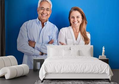 Middle age hispanic couple standing over blue background happy face smiling with crossed arms looking at the camera. positive person. Wall mural