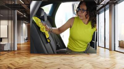 Middle age hispanic woman cleaning car interior with microfiber cloth at car wash station Wall mural