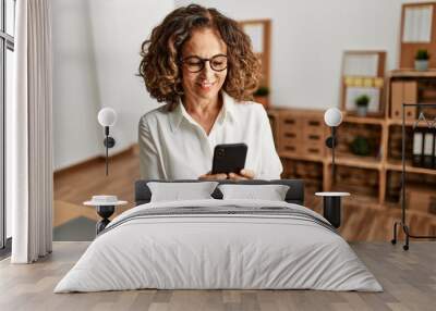 Middle age hispanic woman smiling confident using smartphone at office Wall mural