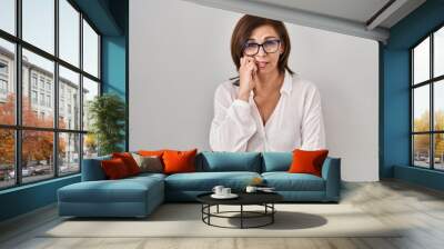 Middle age hispanic woman standing over isolated background looking stressed and nervous with hands on mouth biting nails. anxiety problem. Wall mural