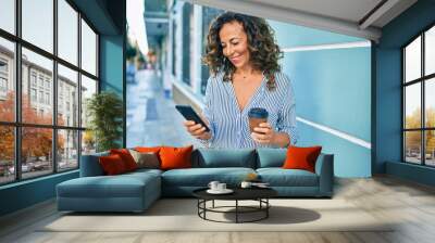 Middle age hispanic woman using smartphone and drinking take away coffee at the city. Wall mural