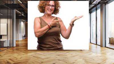 Middle age hispanic woman wearing glasses over isolated background amazed and smiling to the camera while presenting with hand and pointing with finger. Wall mural