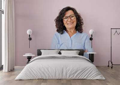 Middle age hispanic woman wearing glasses standing with crossed arms over isolated pink background Wall mural