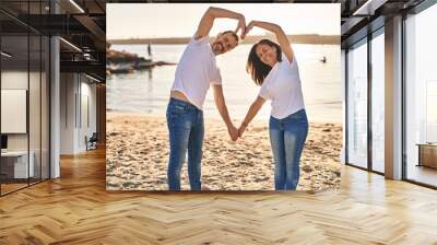 Middle age man and woman couple doing heart symbol with arms at seaside Wall mural