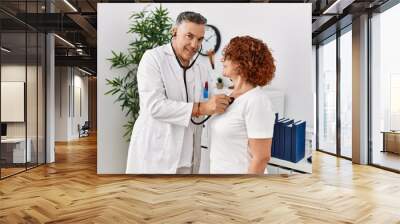 Middle age man and woman wearing doctor uniform auscultate heart having medical consultation at clinic Wall mural