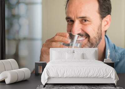 Middle age man drinking a glass of water with a happy face standing and smiling with a confident smile showing teeth Wall mural