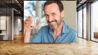 Middle age man drinking a glass of water with a happy face standing and smiling with a confident smile showing teeth Wall mural