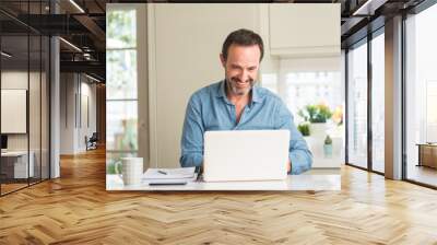 Middle age man using laptop at home with a happy face standing and smiling with a confident smile showing teeth Wall mural